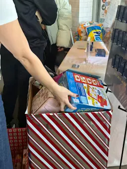 A participant placing a wrapped gift into a HudHaus toy donation box