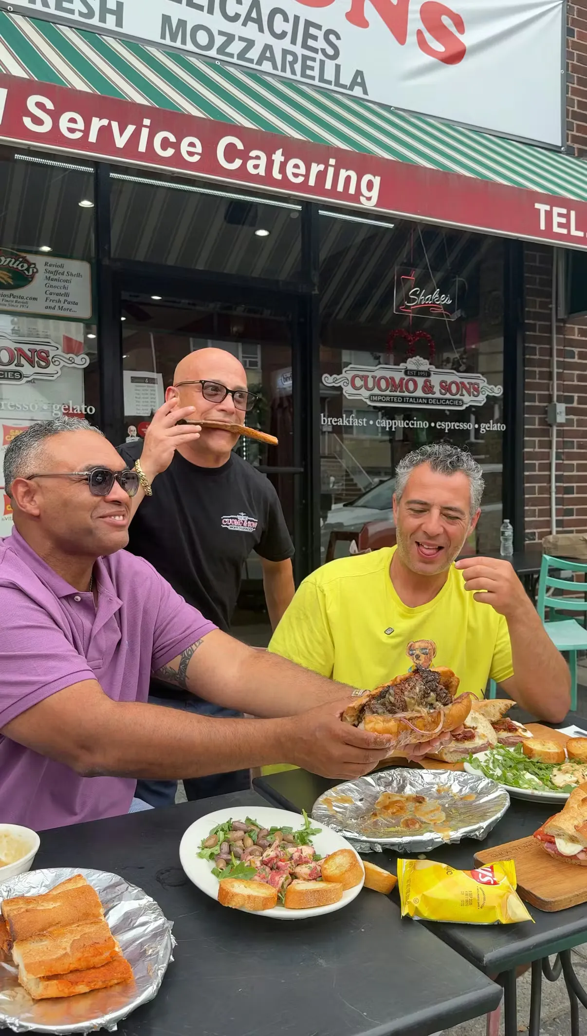 Two friends holding sandwiches in front of the Cuomo & Sons storefront in North Bergen